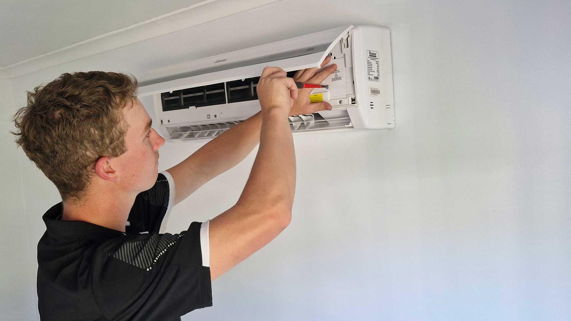 A Man Adjusts An Air Conditioner In A Room For Effective Cooling — Oceanside Services In Burleigh Heads, QLD