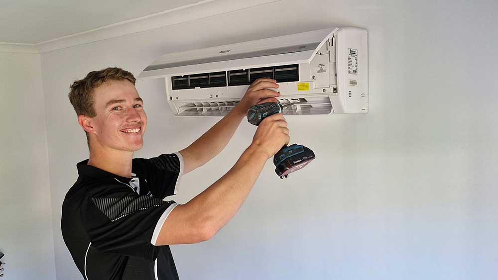 A Man Fixes An Air Conditioner In A Room To Restore Cool Air — Oceanside Services In Burleigh Heads, QLD