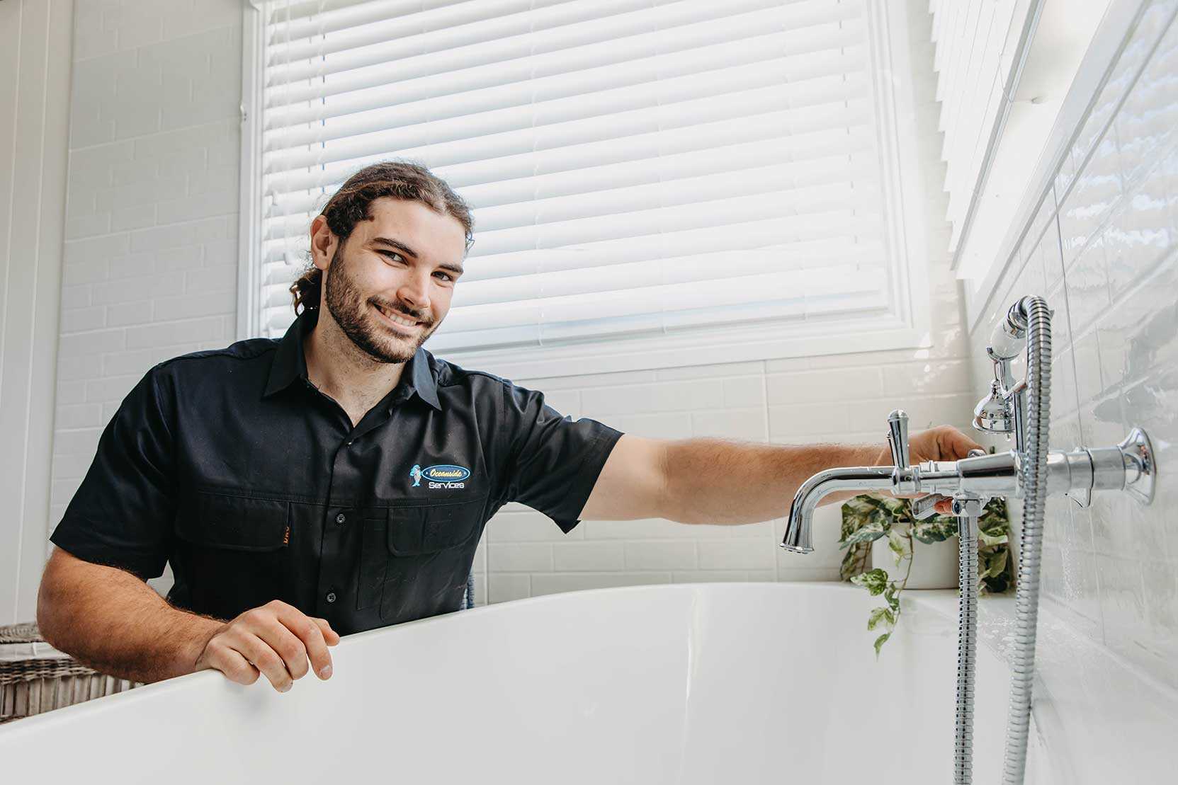 A Man In A Black Shirt Stands Near A Bathtub, Highlighting A Modern Bathroom — Oceanside Services In Burleigh Heads, QLD